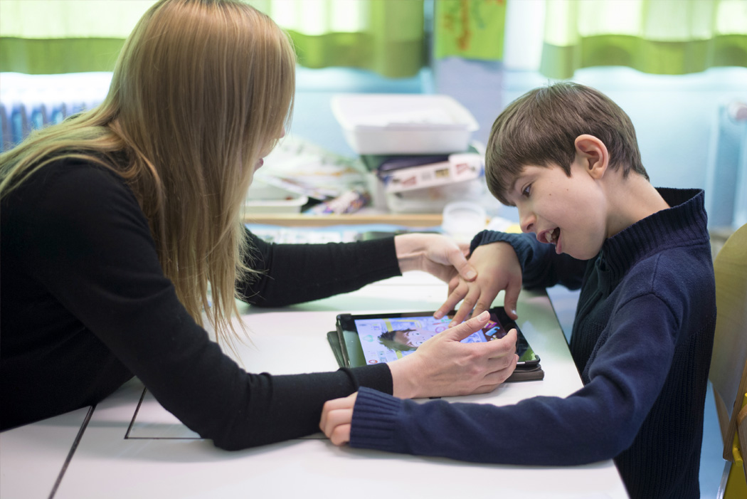 un jeune autiste travaille sur une tablette avec une assistante