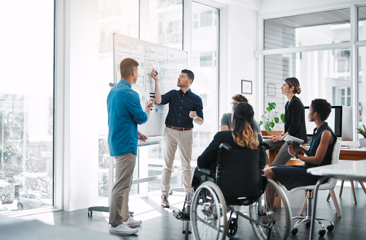 Réunion d'équipe avec hommes et femmes debout, une personne en fauteuil