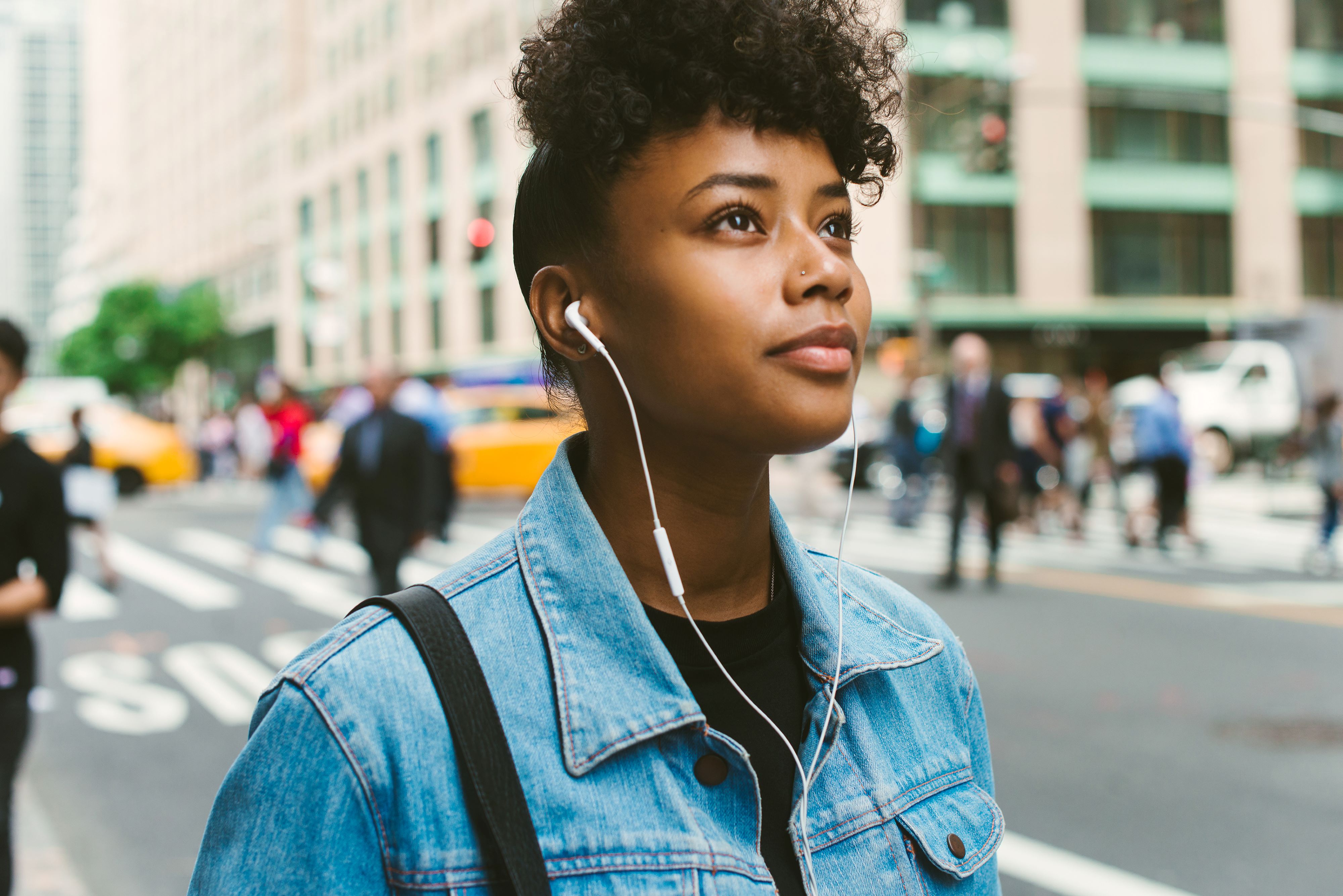 Jeune femme avec ses écouteurs dans les oreilles contemplative dans une rue