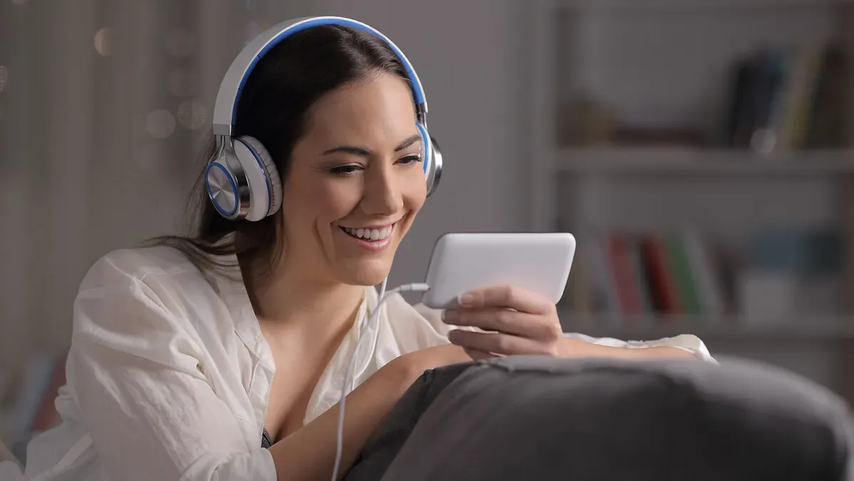 Femme avec un casque audio sur les oreilles, souriant devant son écran