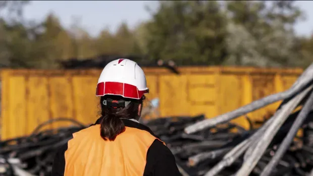 Technicienne orange devant une pelleteuse qui ramasse des cables
