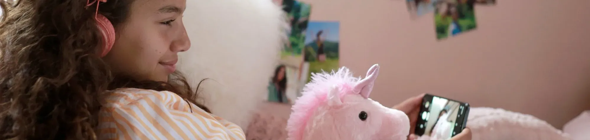 Une jeune fille avec doudou rose regarde un mobile dans sa chambre