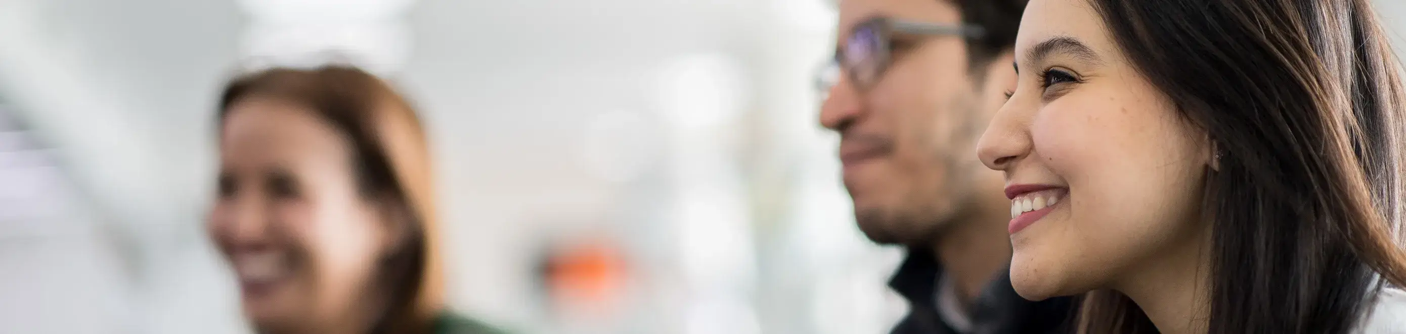 1 femme premier plan souriante et 2 hommes floutés en arrière plan 