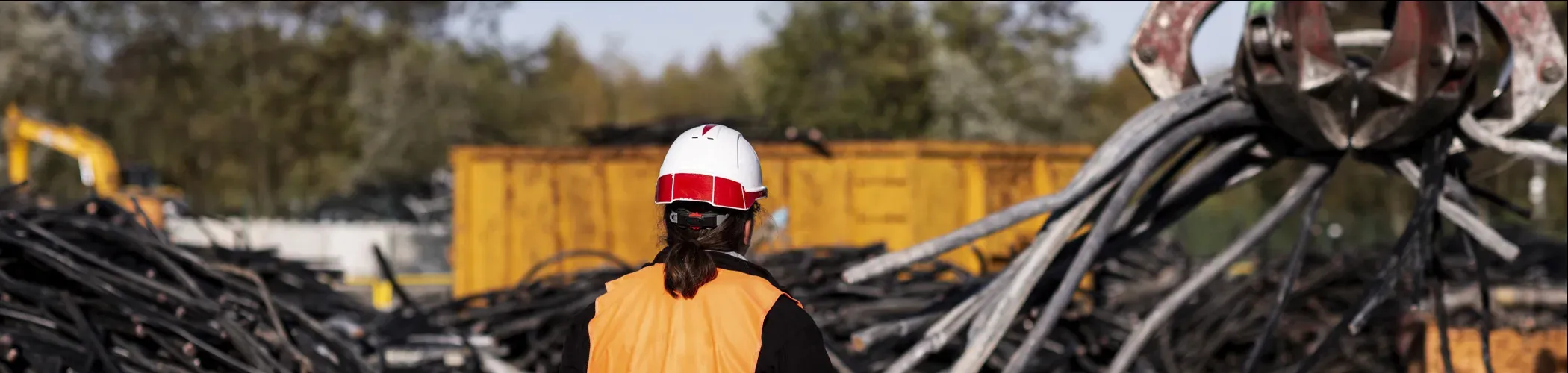 Technicienne orange devant une pelleteuse qui ramasse des cables