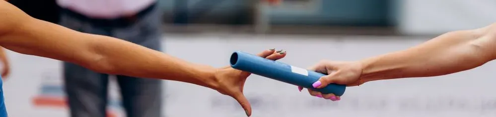 1 main féminime passe le bâton de relai dans une autre main