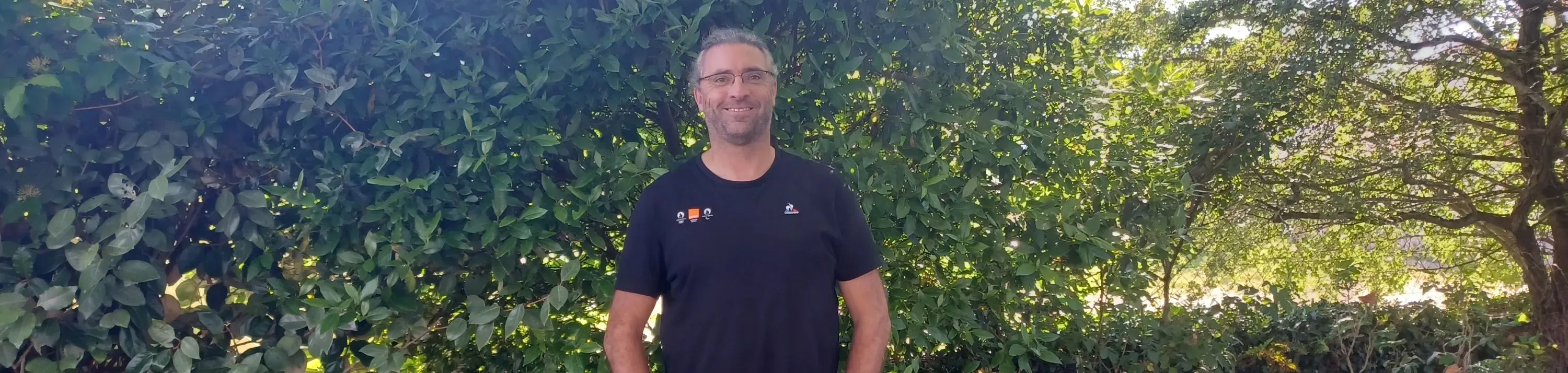 Cédric, Network Expert, smiling in front of a bush 