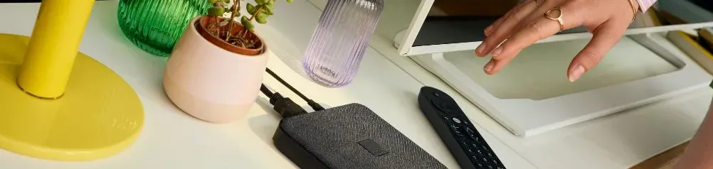 Une main tendue vers un décodeur TV Oranhge et une télécommande dans un salon