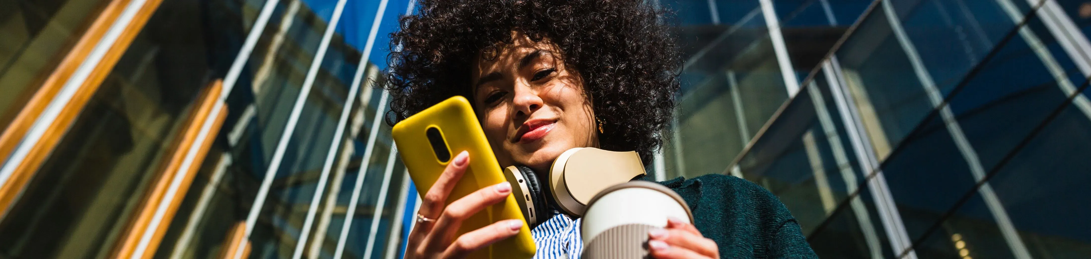 Femme tenant un smartphone jaune en contreplongée entre des buildings