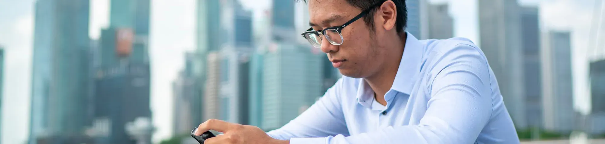 Un homme asiatique consulte son mobile devant un paysage de buildings