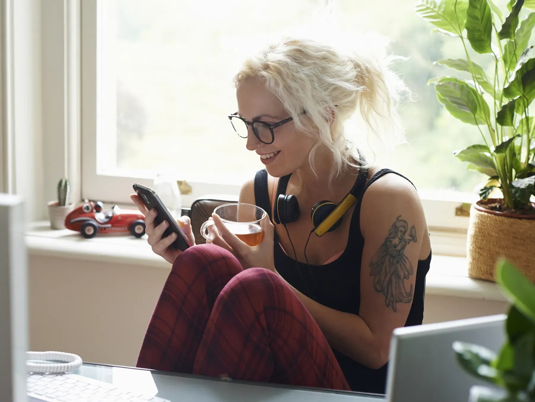 Femme assise en face de son bureau à domicile, souriant devant son téléphone