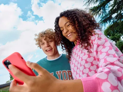 2 jeunes sourient devat l'écran d'un mobile dans un parc