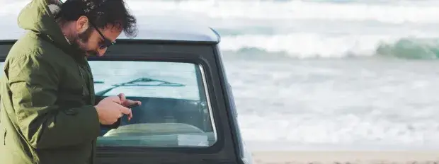 Homme consulte son mobile sur la plage devant sa voiture