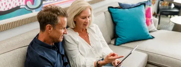 Un homme et une femme âgées sur un canapé regarde une tablette